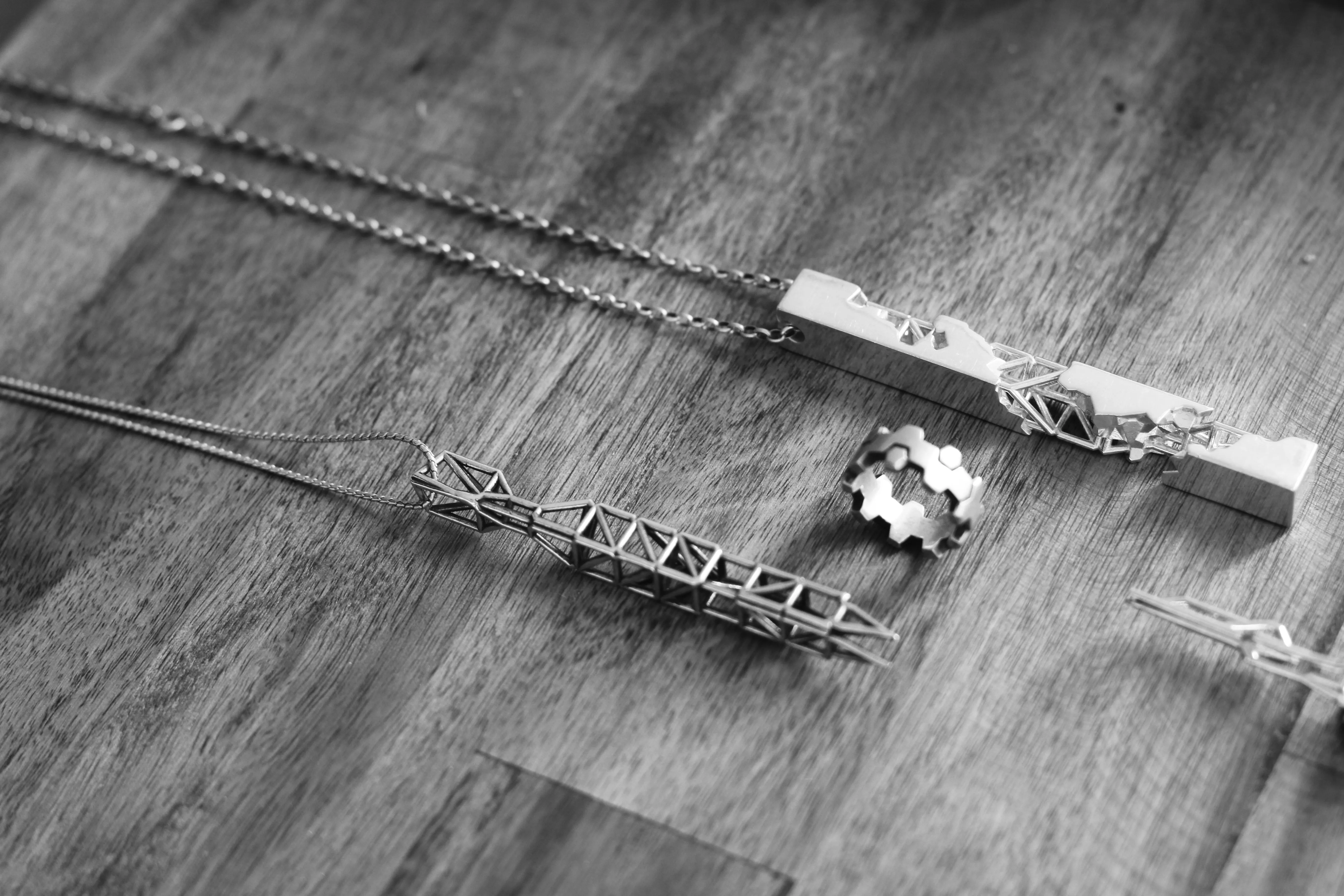 A group of silver pendants and a ring whose forms combine solid architectural profiles with open triangulated lattices.