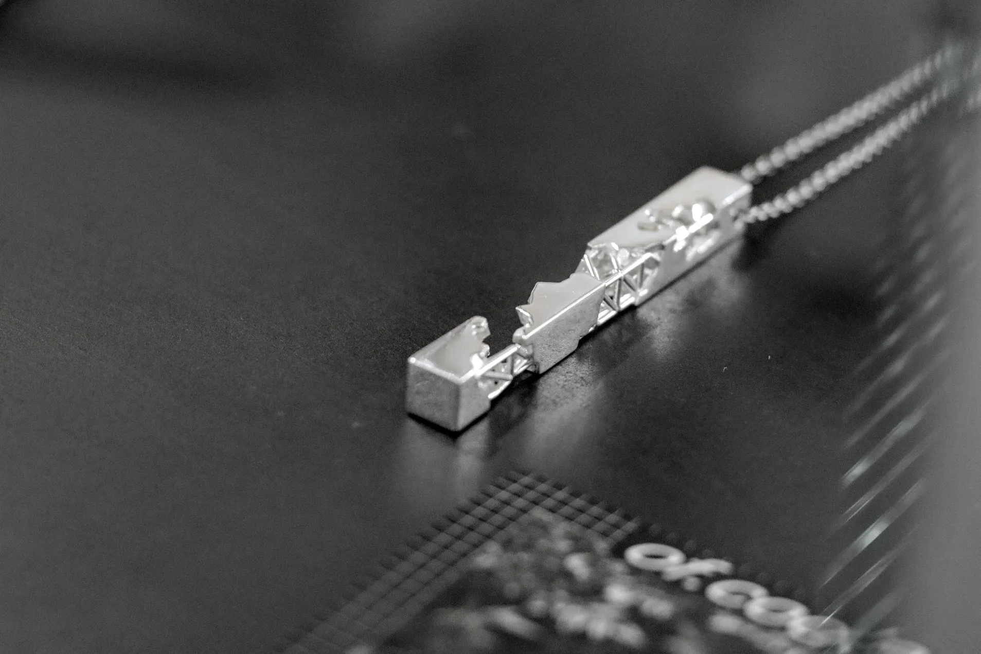 Close view of a silver bar pendant combining solid stepped planes with an exposed internal truss along its underside.