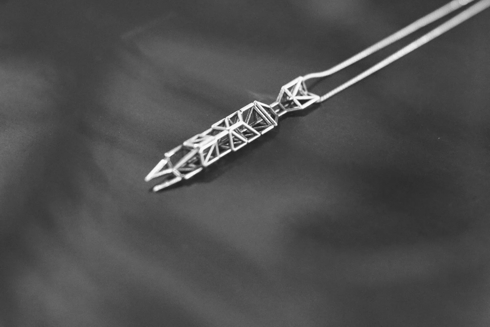 Close view of the silver truss pendant, showing the triangulated web between its top and bottom chords and the tapered points at each end.